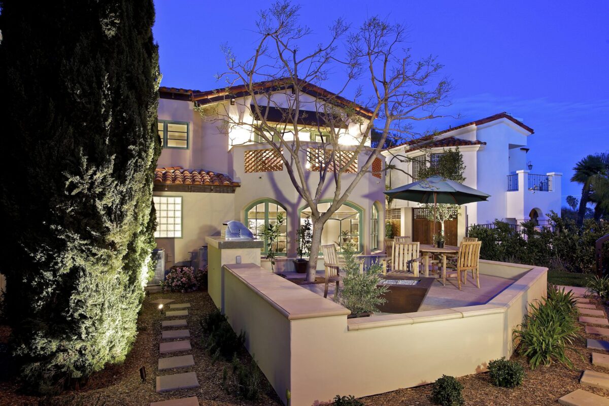 A cozy two-story house at dusk with outdoor seating and greenery.